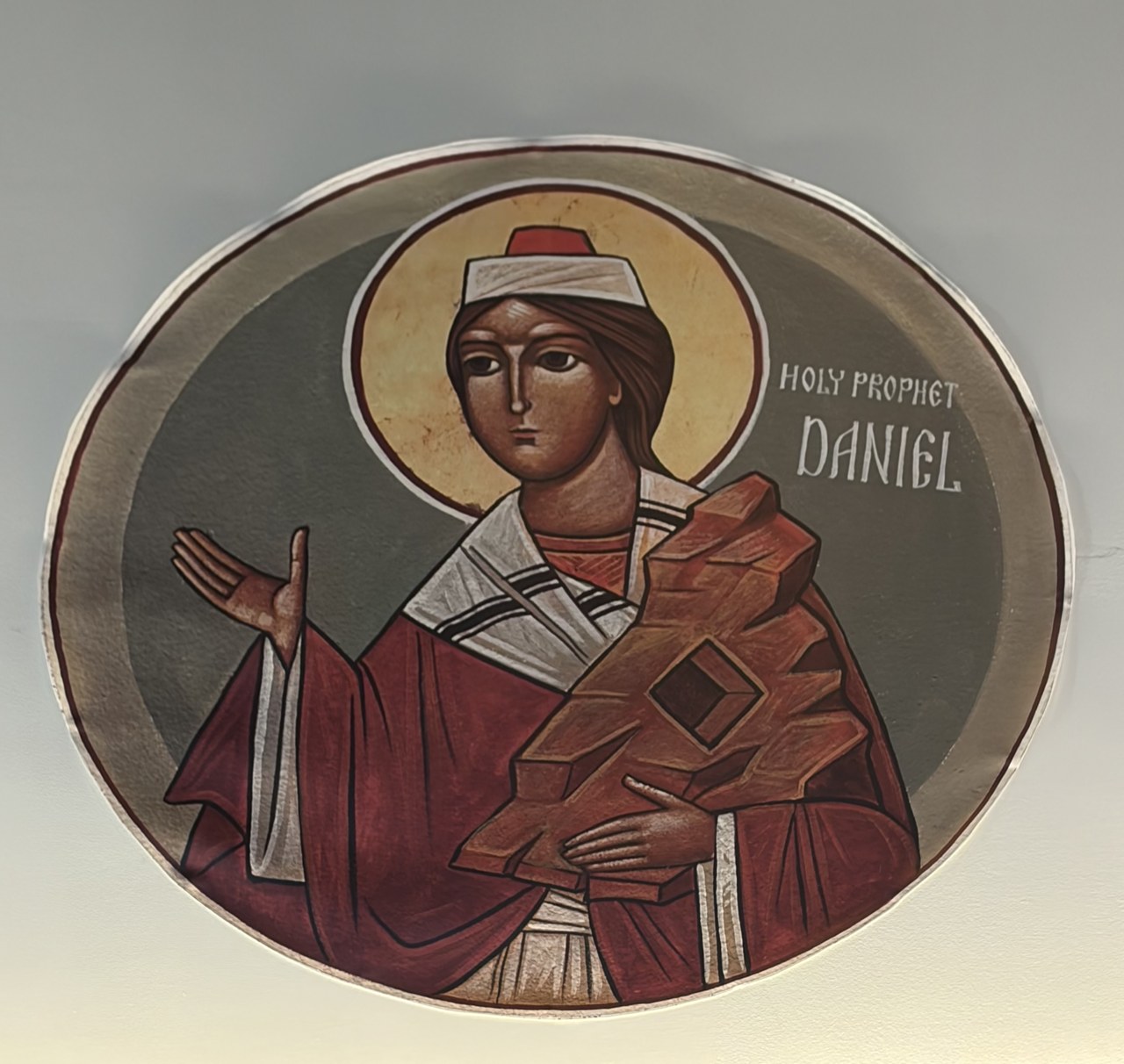 Circular church icon of the prophet Daniel wearing red and holding a mountain-shaped stone.